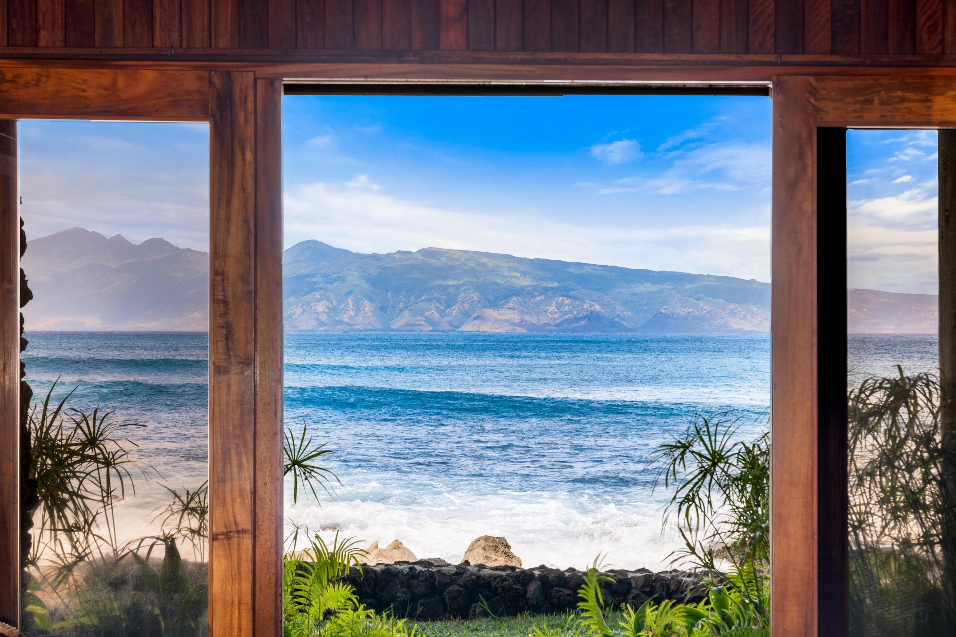 The ocean framed floor-to-ceiling between the home's timber posts, Molokai on the horizon