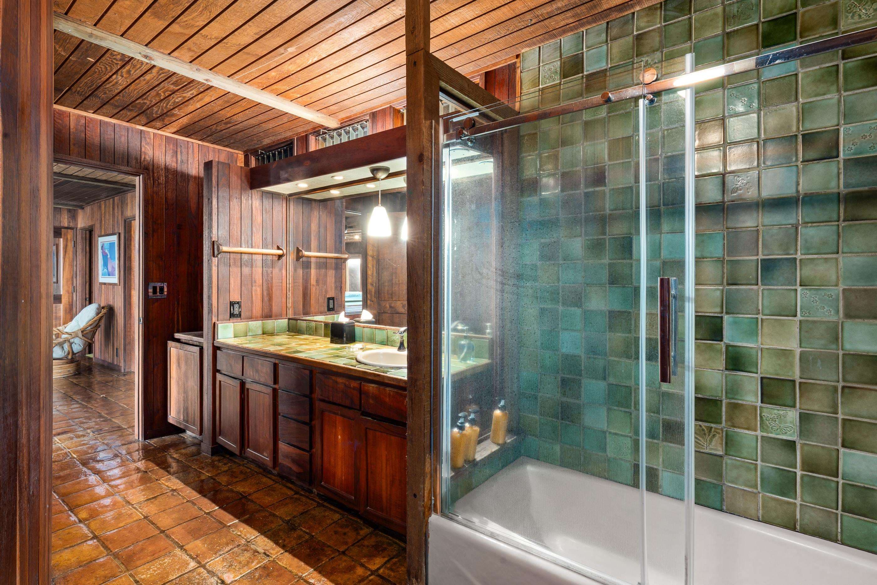 Bathroom with a glass-door shower in sea-green tile and a long koa vanity