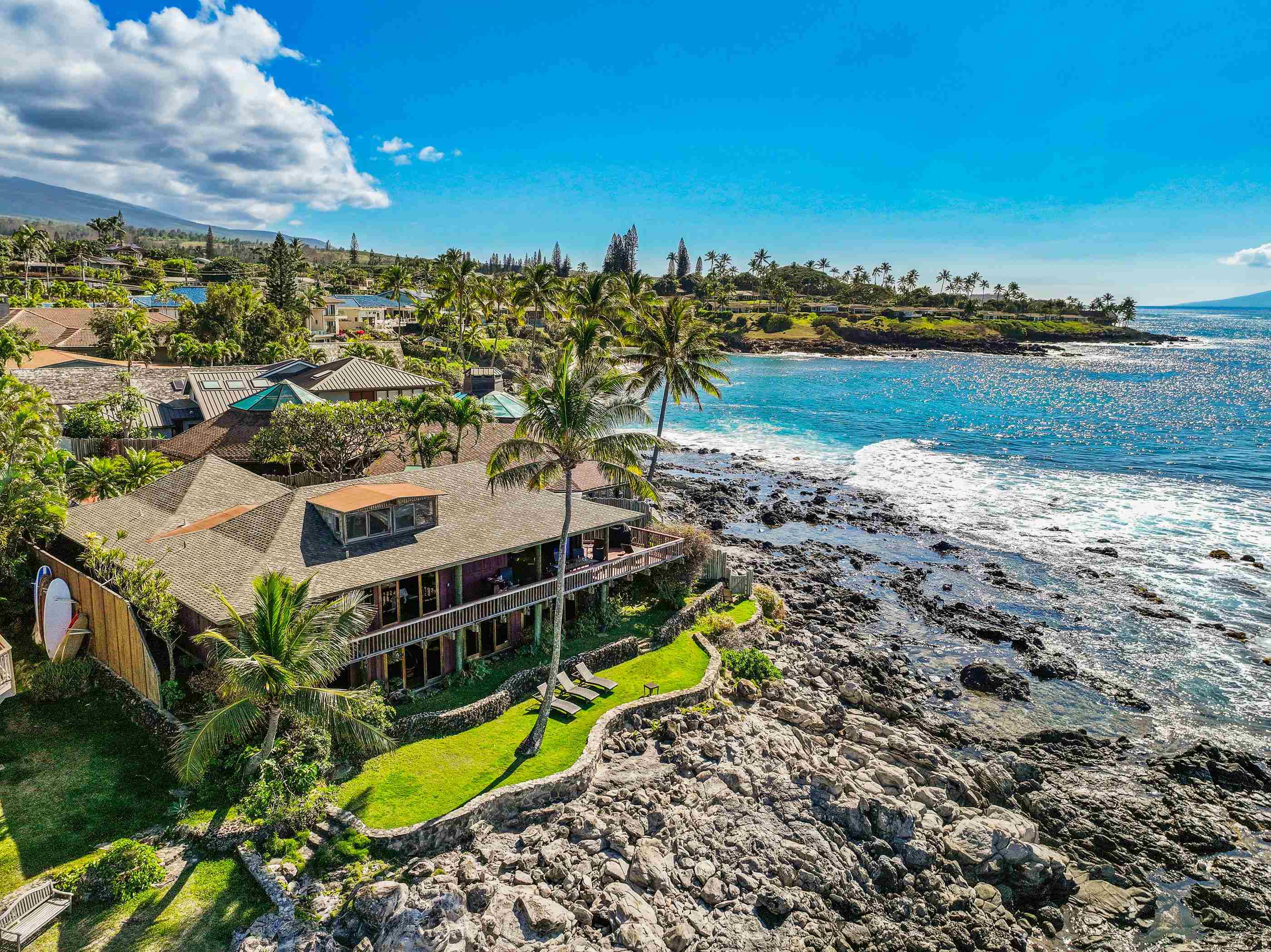 Low aerial over the point: the house on its lawn at the water's edge, the coastline curving away behind