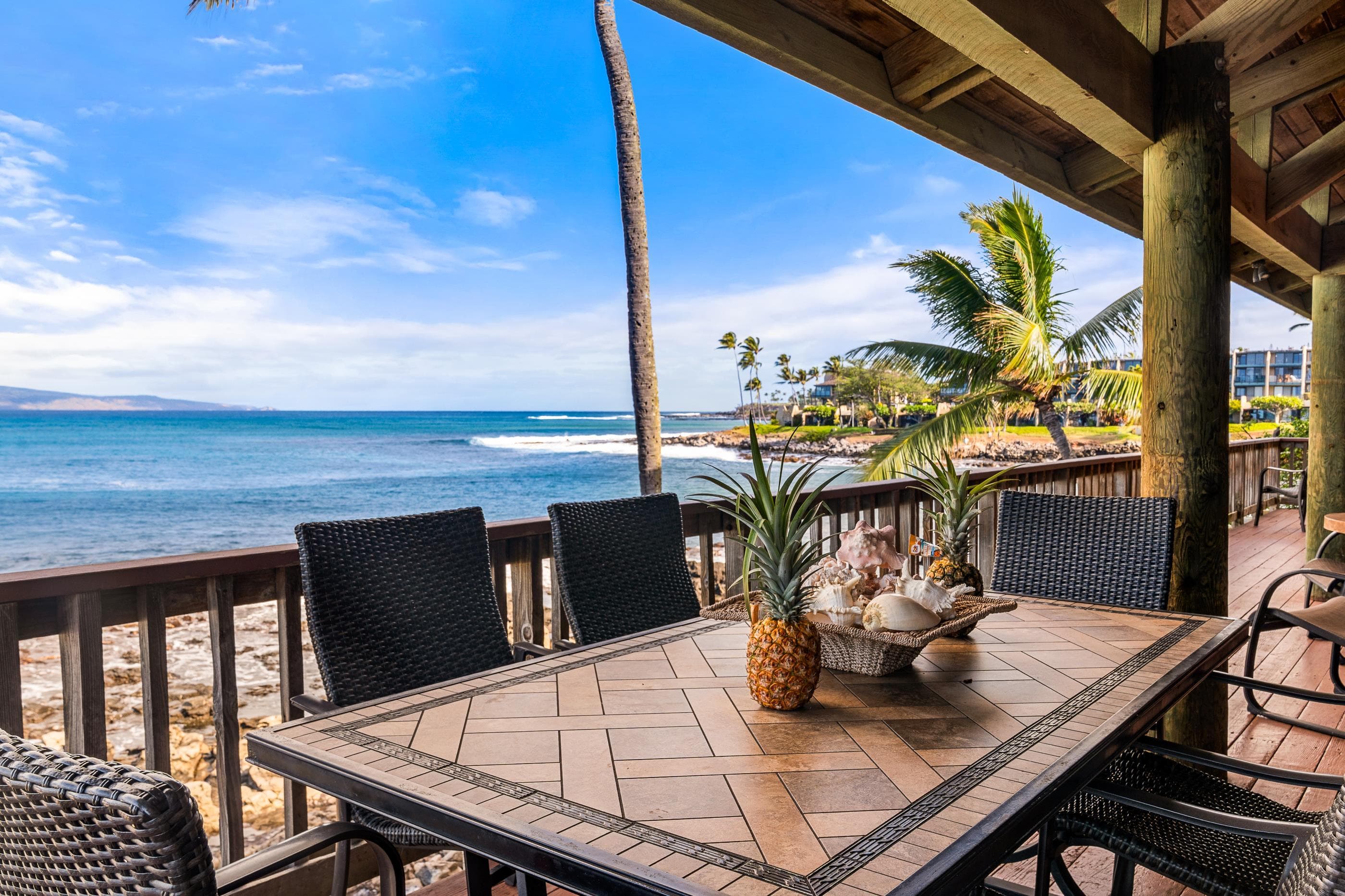 Deck dining table with a pineapple centerpiece, the beach and headland stretching out beyond the railing
